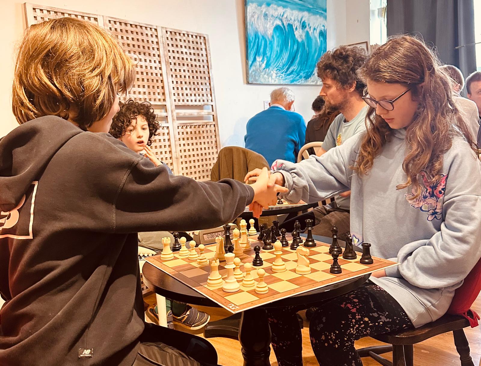 Two junior players shaking hands over the board at the club